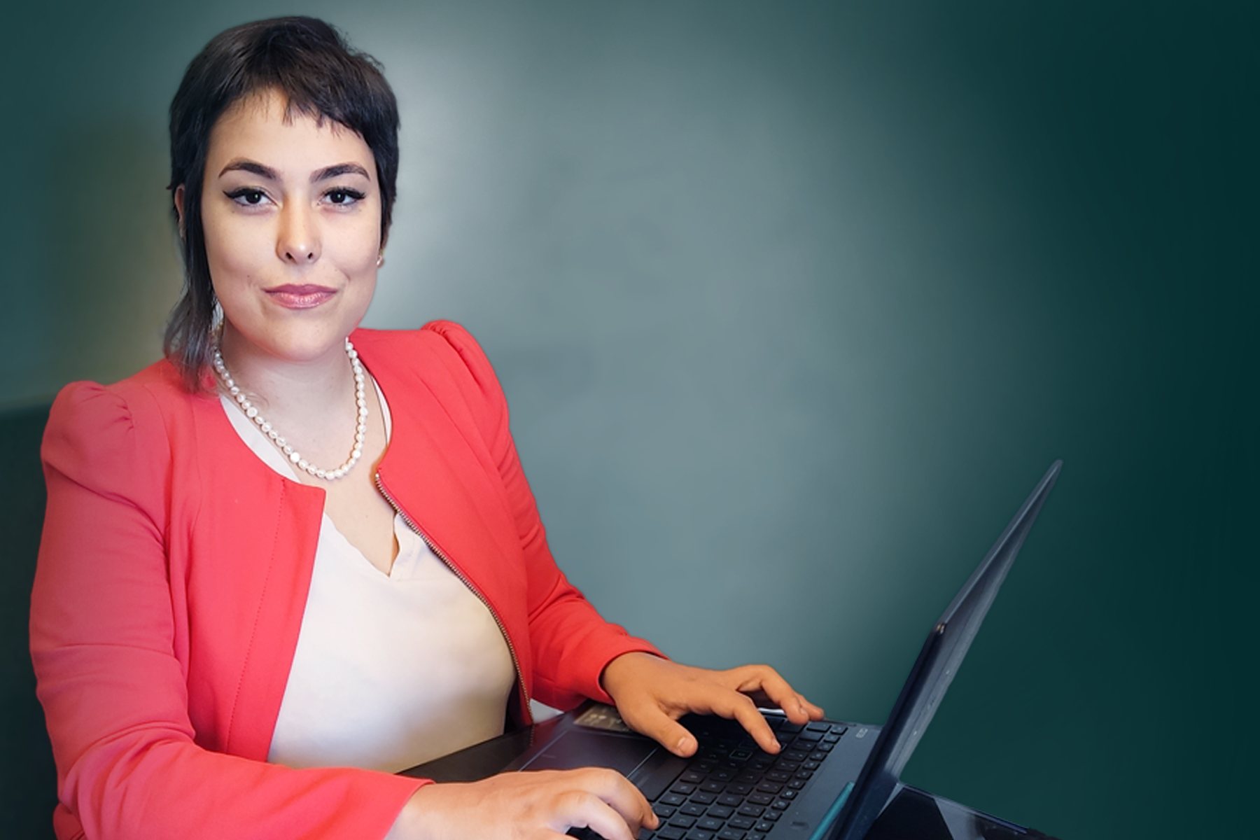 Dra. Francieli Zambonini, de blazer coral, trabalhando ao computador